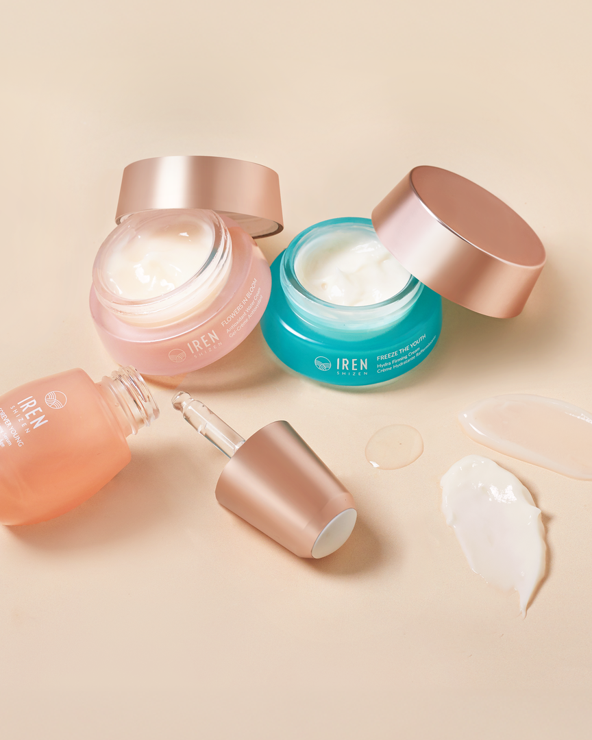 The MOCHI SKIN Instant Glow Travel Set by Fast Bundle features three skincare products in glass jars and a dropper bottle with rose gold lids, open to reveal cream and serum, displayed on a beige surface with product smears nearby.