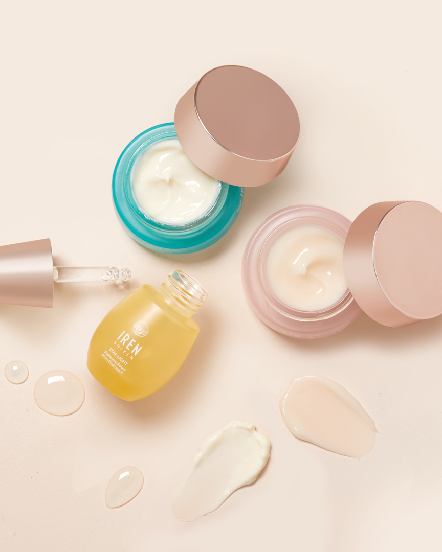 Top view of the MOCHI SKIN Instant Glow Travel Set by Fast Bundle: two open jars (blue and pink) and a yellow serum bottle with dropper, surrounded by cream and serum smears on a light background.