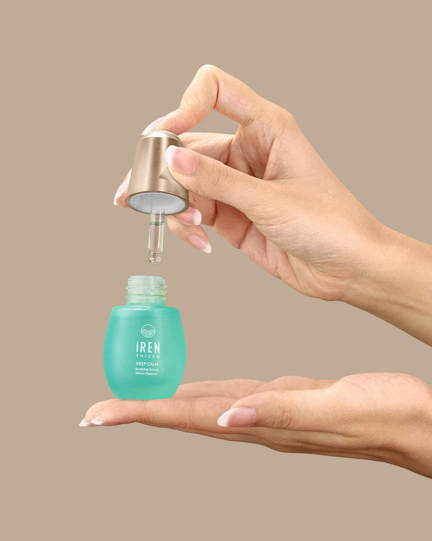 A woman's hand holding a bottle of customised KEEP CALM Soothing Serum by IREN Shizen, inspired by Japanese and onsen skincare.