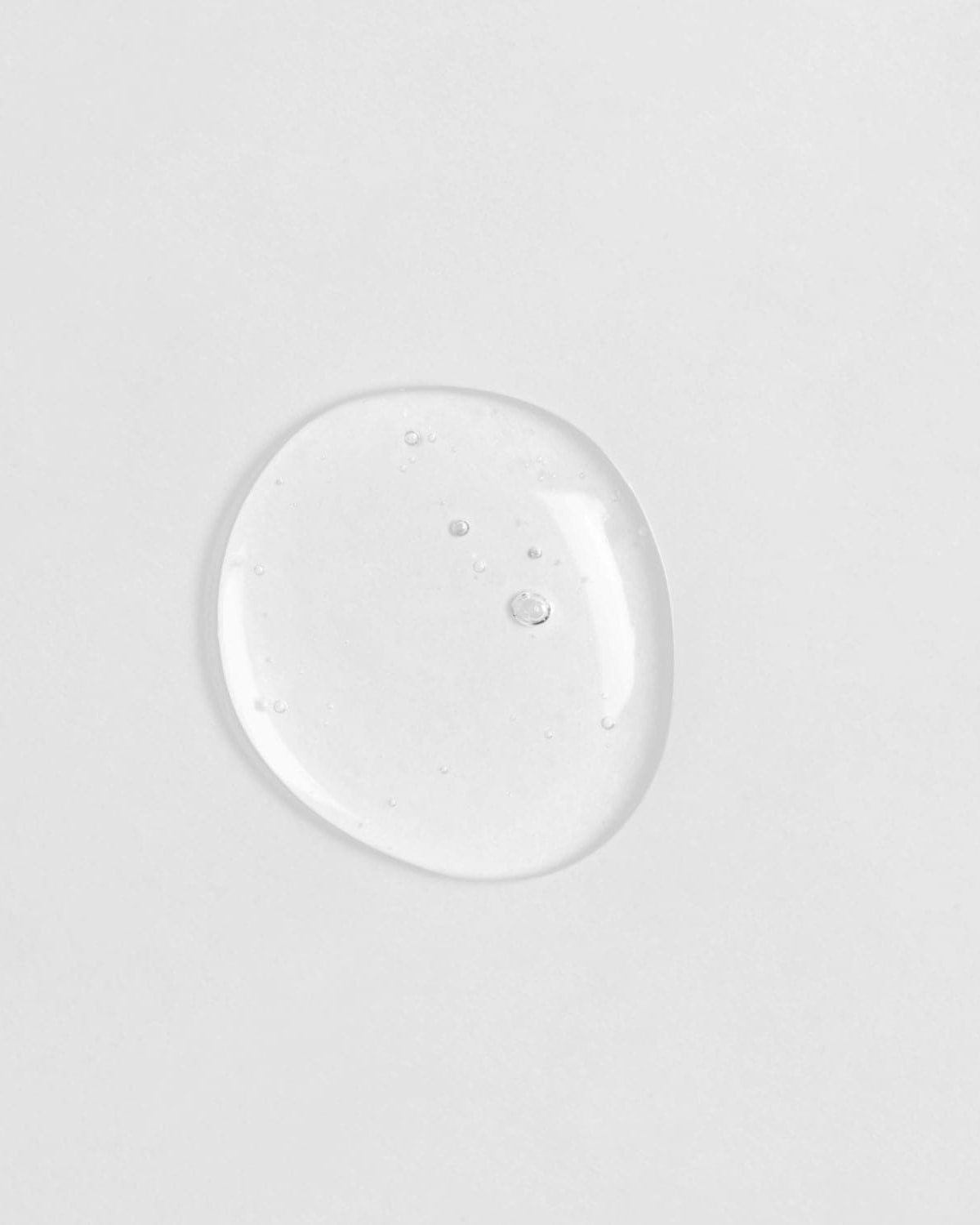 A small drop of Japanese skincare, IREN Shizen GLOW-GETTER Renewal Serum, on a white surface.