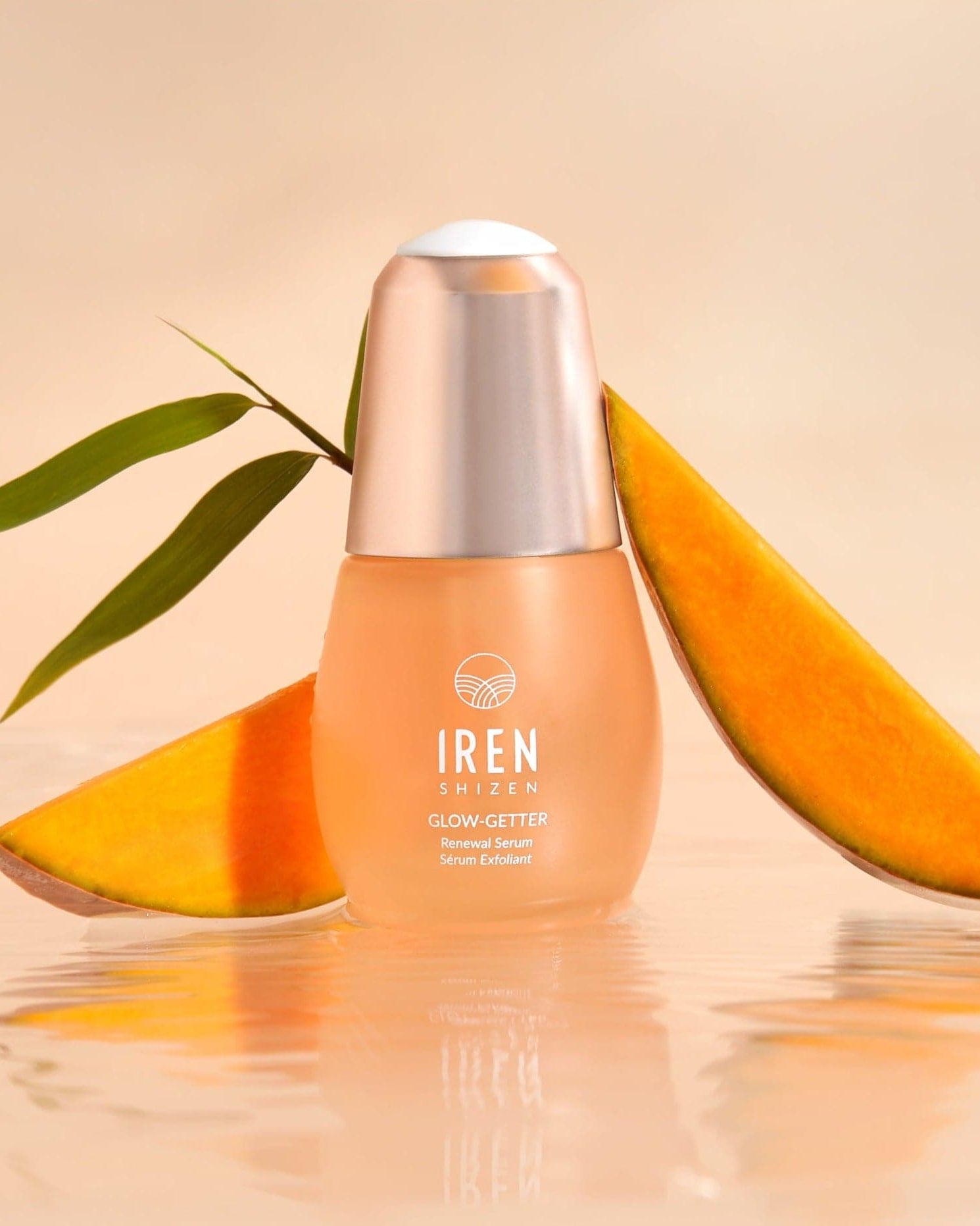 A bottle of custom Japanese skincare, IREN Shizen GLOW-GETTER Renewal Serum, next to a slice of mango.