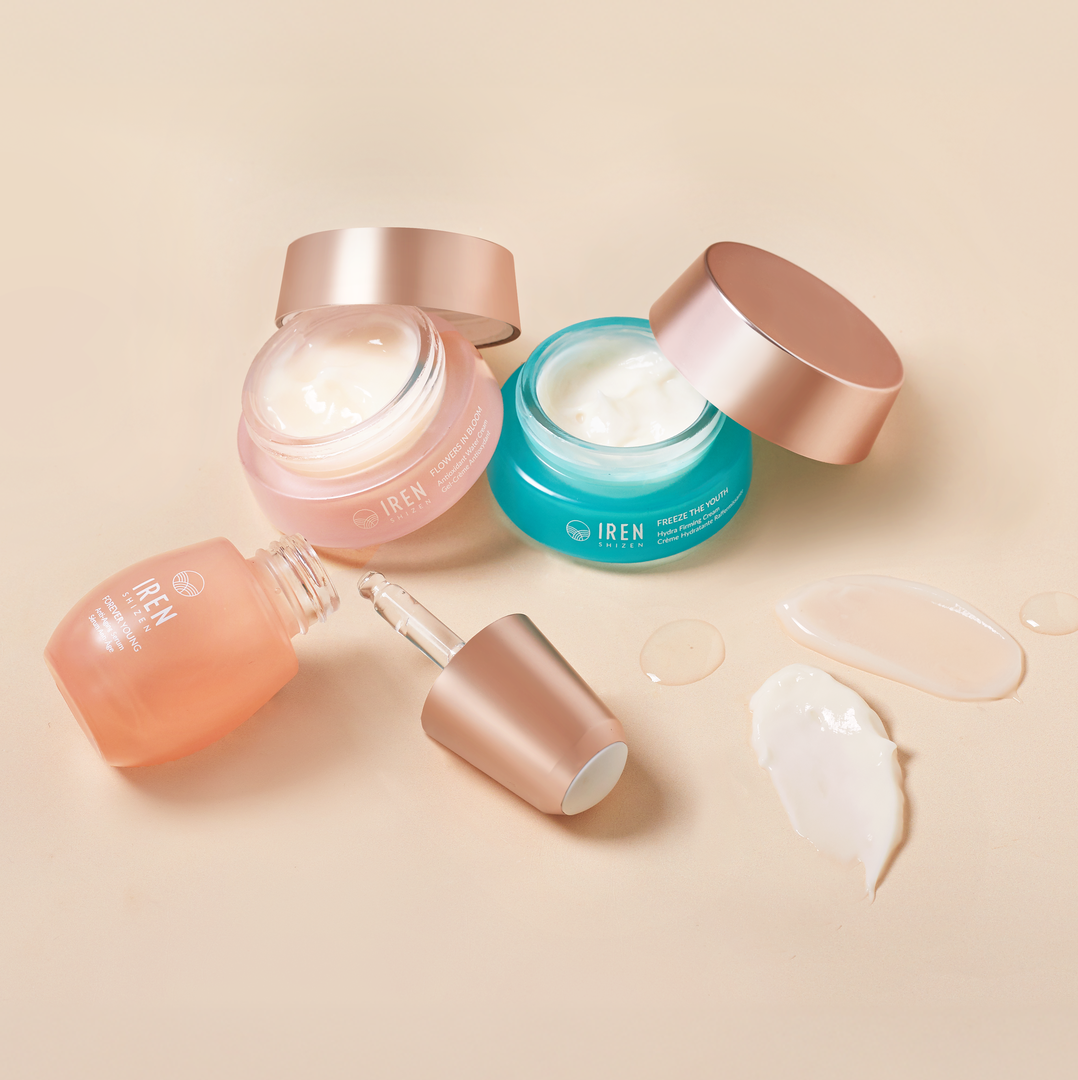 The MOCHI SKIN Instant Glow Travel Set by Fast Bundle features three skincare products in glass jars and a dropper bottle with rose gold lids, open to reveal cream and serum, displayed on a beige surface with product smears nearby.