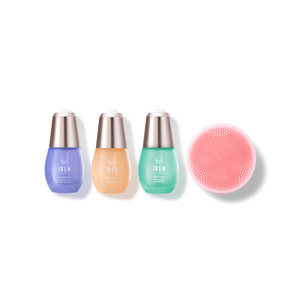 Three bottles of IREN Shizen CLEAR UP PRO Skin Genie Pro + Anti-Blemish Set in purple, beige, and green are placed in a row beside a circular pink facial cleansing device, perfect for achieving a glowing complexion.