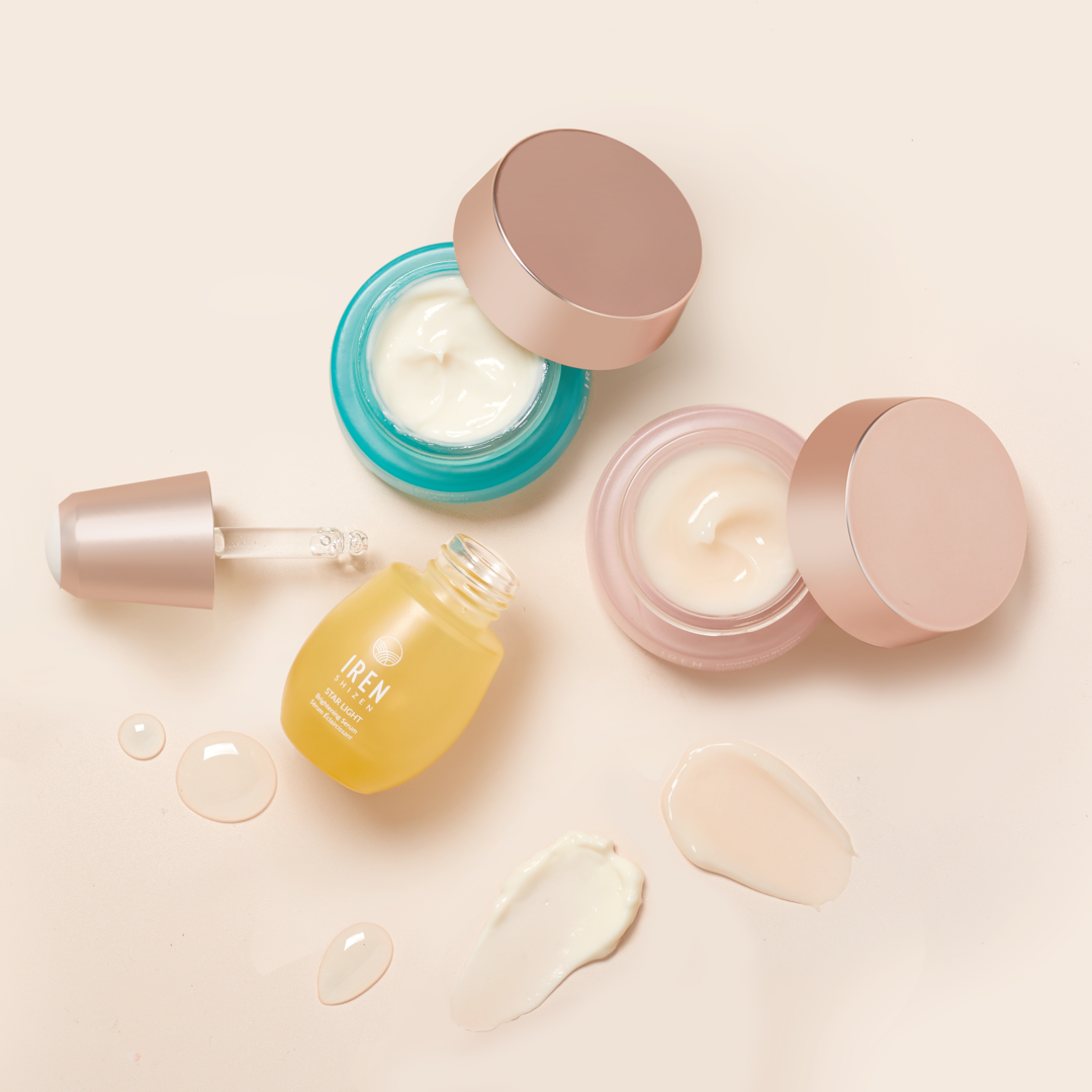 Top view of the MOCHI SKIN Instant Glow Travel Set by Fast Bundle: two open jars (blue and pink) and a yellow serum bottle with dropper, surrounded by cream and serum smears on a light background.