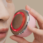 A woman is holding a IREN Shizen SKIN GENIE PRO Cleansing Brush + LED Light Therapy device to her face.