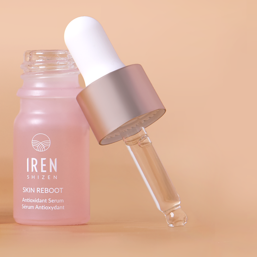 A dropper bottle of TIMELESS ELIXIR Anti-Aging Eye Skincare Kit by IREN Shizen, an anti-aging elixir with Bakuchiol, is shown with the dropper leaning against the open bottle. The pink bottle with a white label is set against a beige background.