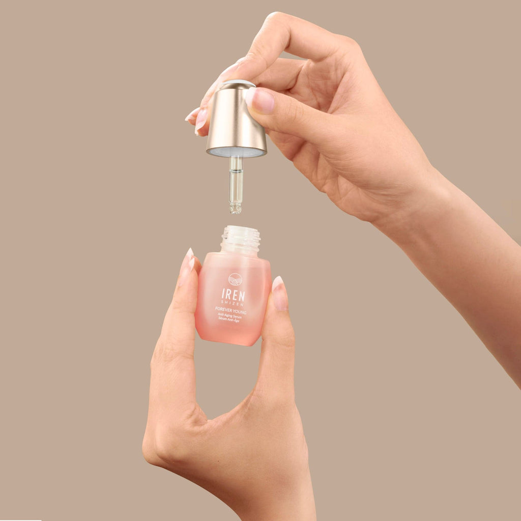 A hand is holding a bottle of IREN Shizen ONSEN AGE DEFENSE Pro-Collagen Set on a beige background.