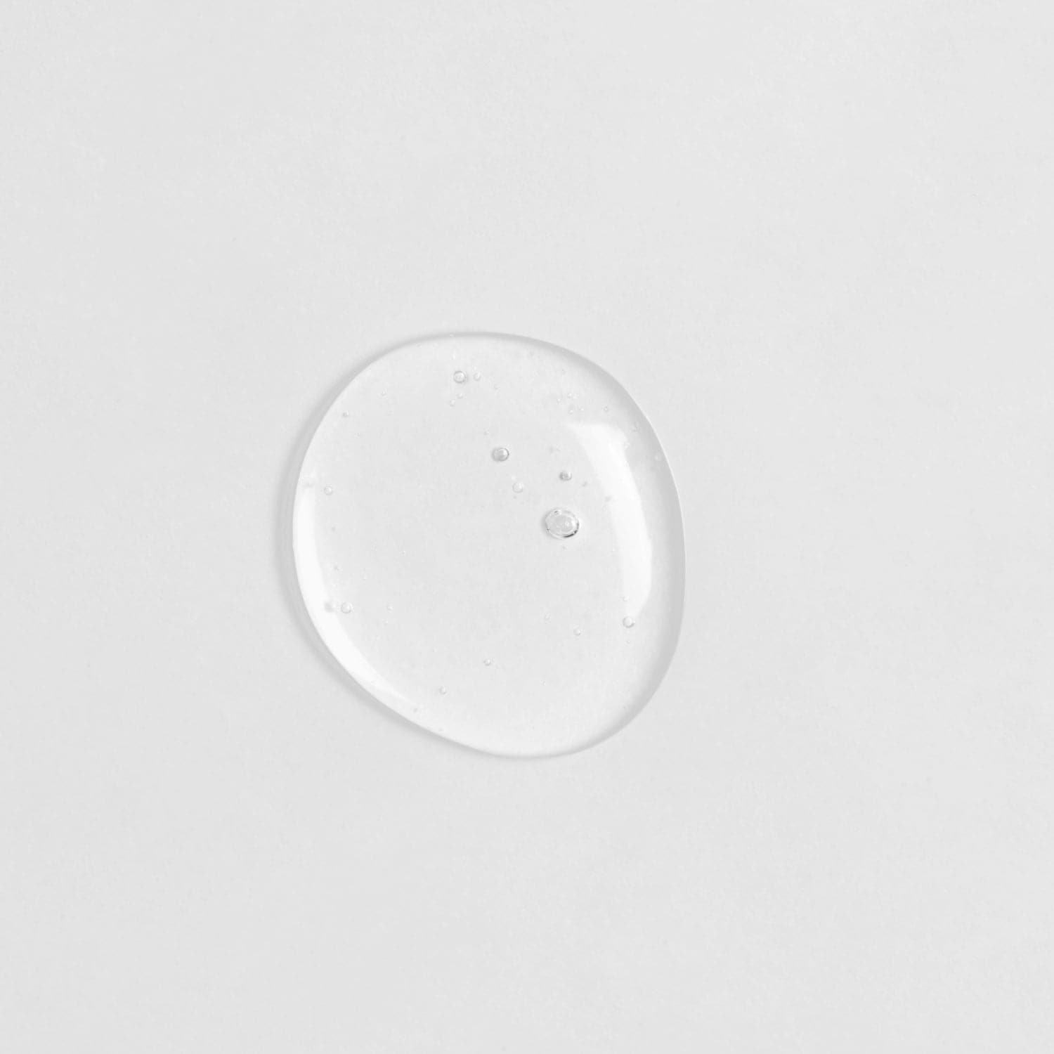 A small drop of Japanese skincare, IREN Shizen GLOW-GETTER Renewal Serum, on a white surface.