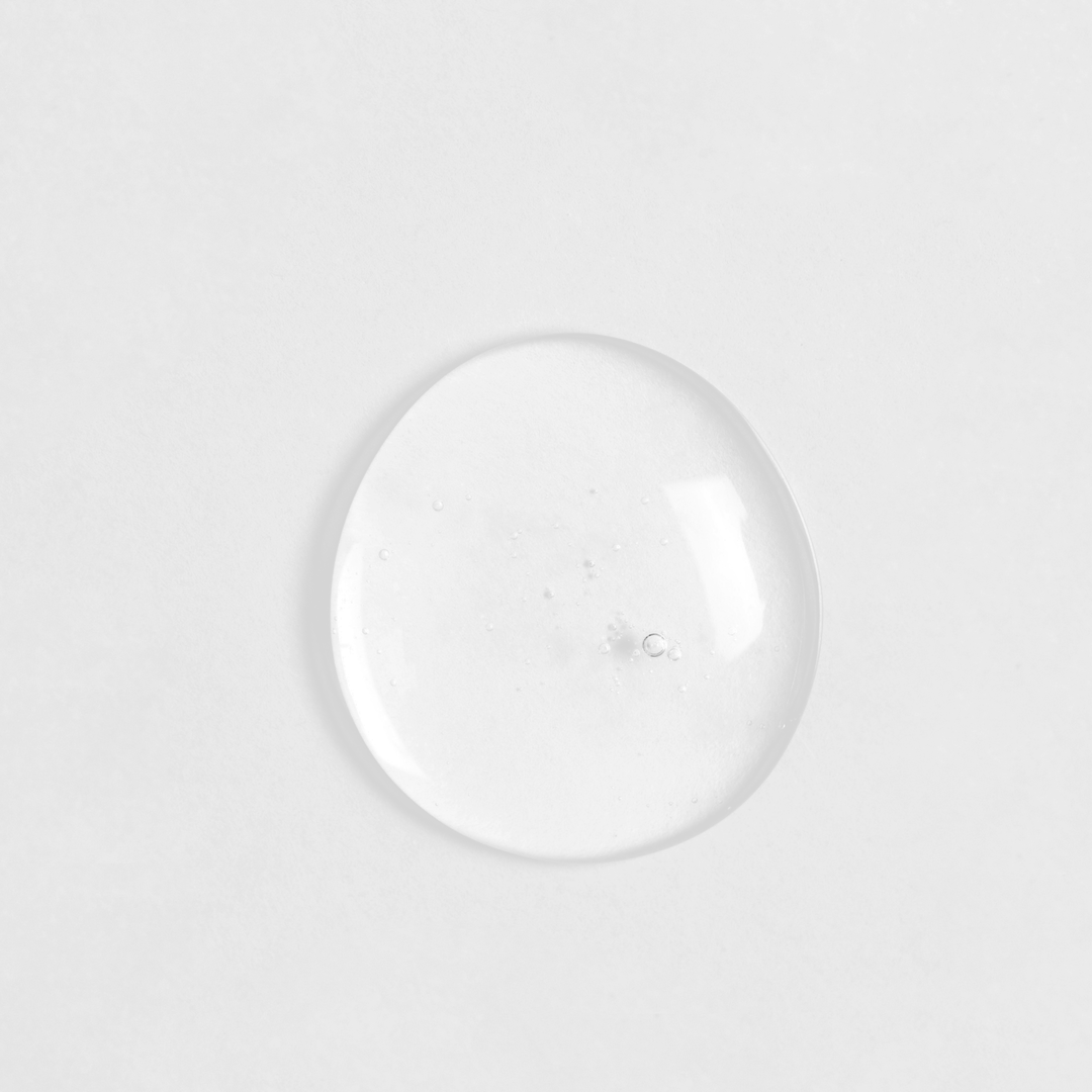 A single, clear droplet of IREN Shizen's LIFT & FIRM Anti-Aging Duo Serum on a white surface.