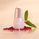 A pink bottle labeled "IREN Shizen APAC TIMELESS ELIXIR Anti-Aging Eye Skincare Kit" sits elegantly on a glossy surface, surrounded by pomegranate seeds and a green leaf, epitomizing the essence of premium anti-aging serums.